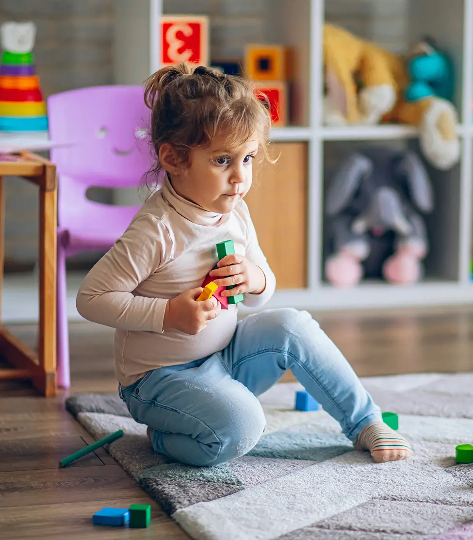 Niña pequeña jugando con bloques de madera en el suelo
