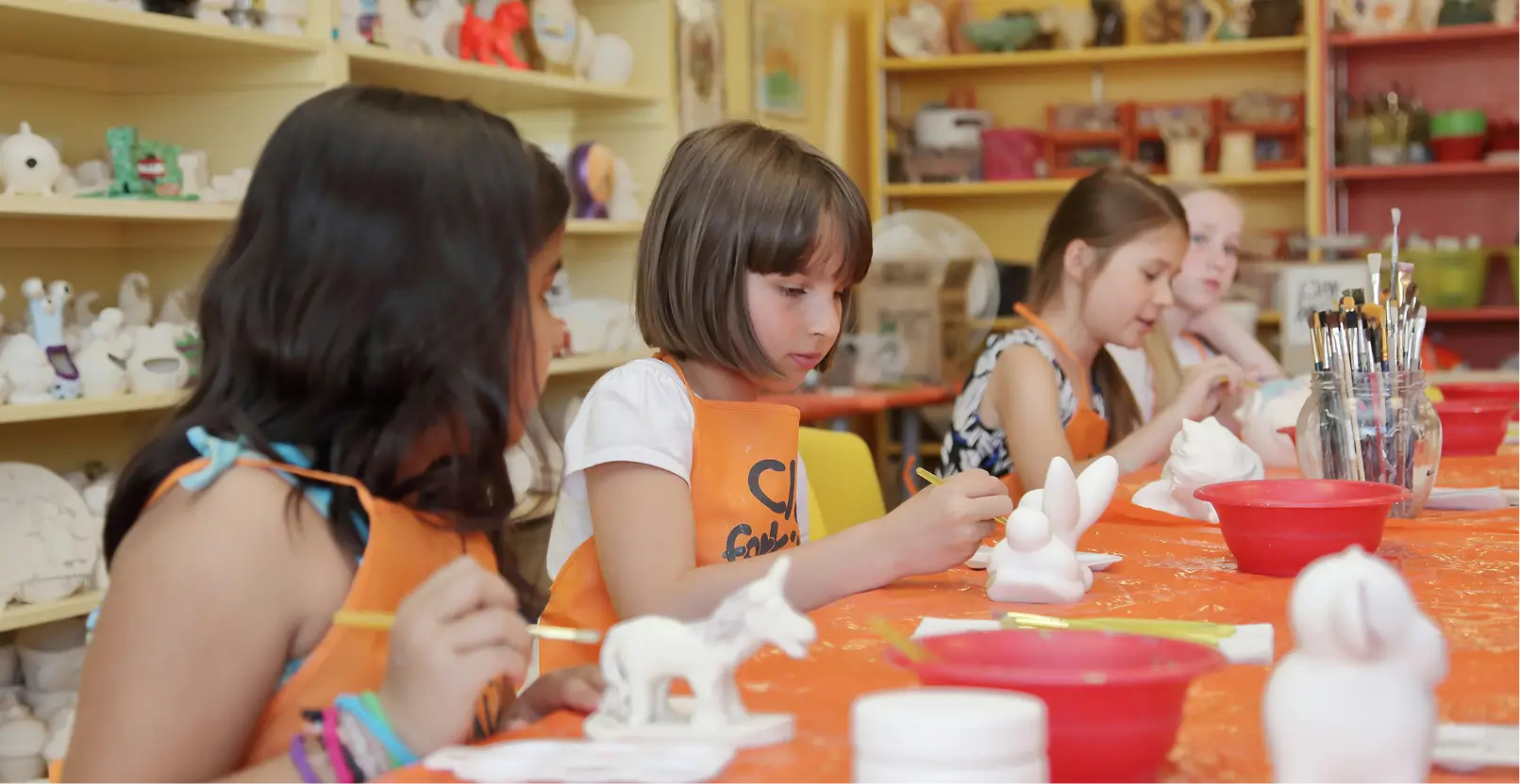 Grupo de niñas pintando figuras de cerámica en un taller